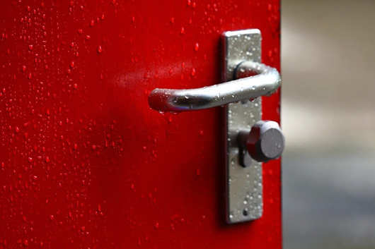 Door handle on a red door that is wet from rain